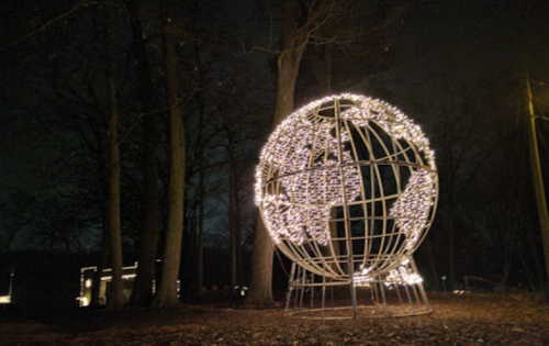 A large globe sculpture wrapped in string lights, surrounded by trees at night.