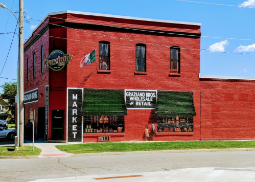 Red brick building with "Graziano Bros Market" sign, featuring wholesale and retail offerings, and a Mexican flag.