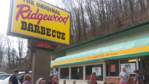 A busy barbecue restaurant with a bright sign reading "The Original Ridgewood Barbecue" and people waiting outside.