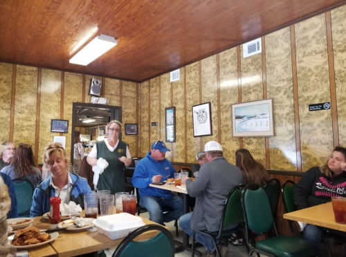 A busy diner with patrons eating, a waitress serving, and rustic decor on the walls.