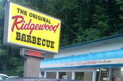 Sign for "The Original Ridgewood Barbecue" with a bright yellow background, surrounded by trees and parked cars.