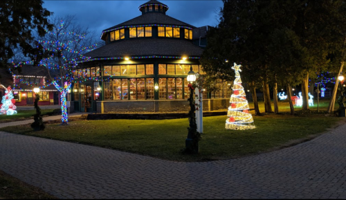 A festive scene featuring a lit gazebo and a decorated Christmas tree, surrounded by colorful holiday lights.