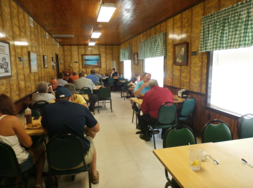 A busy diner with patrons seated at tables, wooden walls, and green checkered curtains.