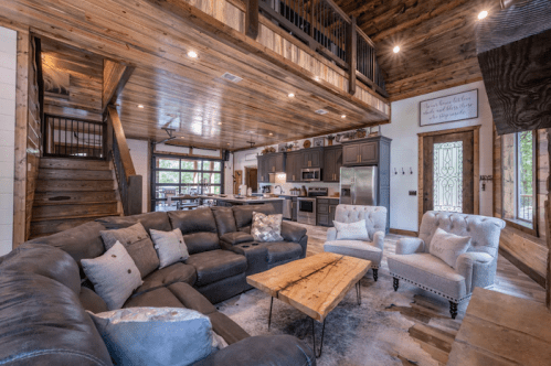 Cozy living room with a large sectional sofa, wooden accents, and a staircase leading to a loft area.