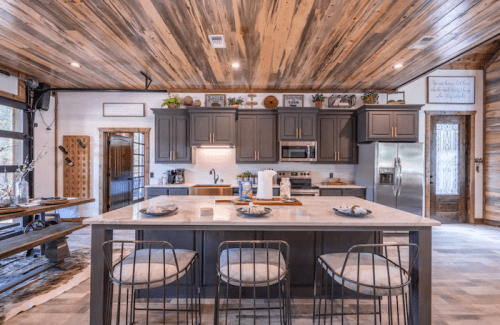 Modern kitchen with dark cabinets, marble island, and wooden ceiling, featuring a cozy dining area and natural light.
