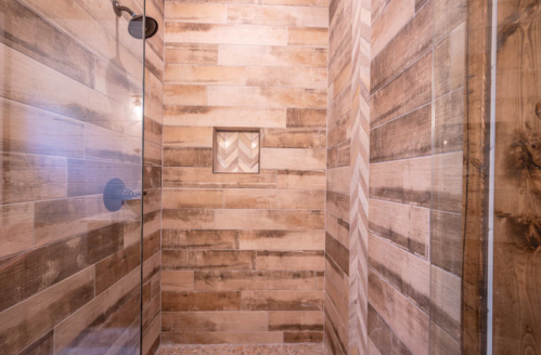 A modern shower with wooden-style tiles and a built-in shelf featuring a chevron pattern.