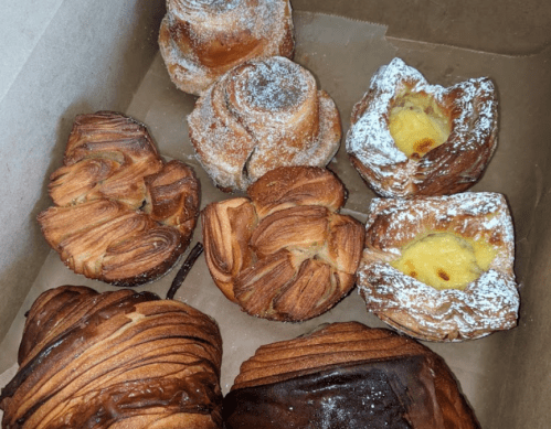 A box of assorted pastries, including croissants, danishes, and sweet rolls, some dusted with powdered sugar.