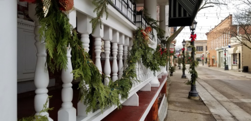 Decorated porch railing with greenery and festive ornaments, overlooking a charming, empty street during the holiday season.