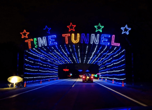 A brightly lit archway reading "TIME TUNNEL" with colorful lights, viewed from a car on a dark road.