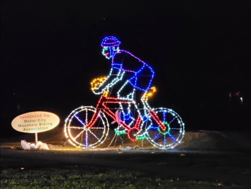 A colorful light display of a cyclist on a bike, set against a dark background, with a sign for a biking association.
