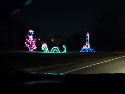 Colorful holiday lights depicting a dinosaur, a castle, and a whimsical character against a dark night sky.