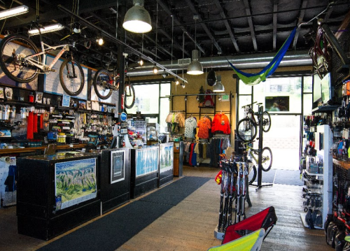 A bike shop interior featuring bicycles, apparel, and accessories, with a welcoming atmosphere and large windows.