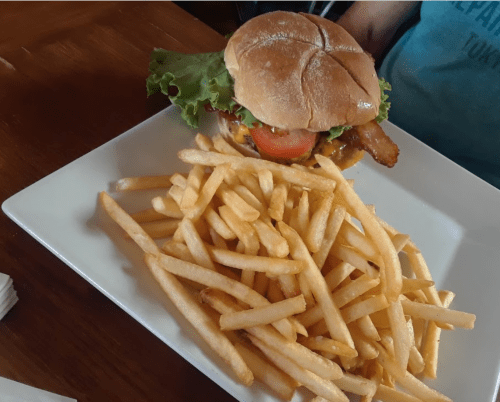 A plate with a burger topped with lettuce, tomato, and bacon, accompanied by a generous serving of French fries.