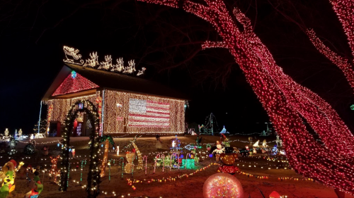 A house decorated with colorful Christmas lights, featuring a large American flag display and festive holiday decorations.
