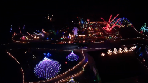 Aerial view of a colorful holiday light display featuring various illuminated shapes and festive decorations at night.