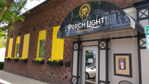 Exterior of Porch Light Coffeehouse, featuring a sign, yellow shutters, and flower boxes under the windows.