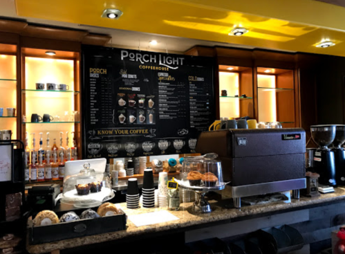 A cozy coffee shop counter with a menu board, coffee machine, pastries, and various coffee supplies.