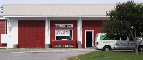 A red barn-style building with a sign reading "Used Books" and a sale banner, alongside a parked white van.