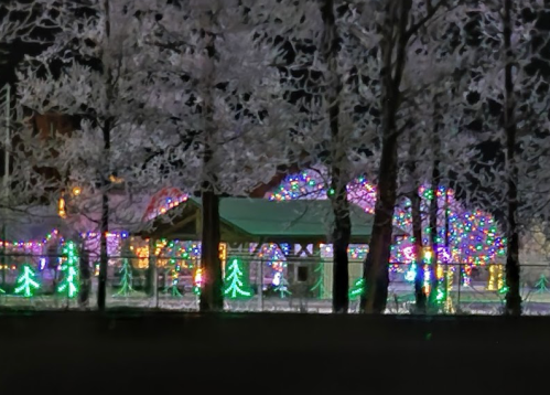 Colorful holiday lights illuminate a snowy scene with trees and a pavilion, creating a festive winter atmosphere.
