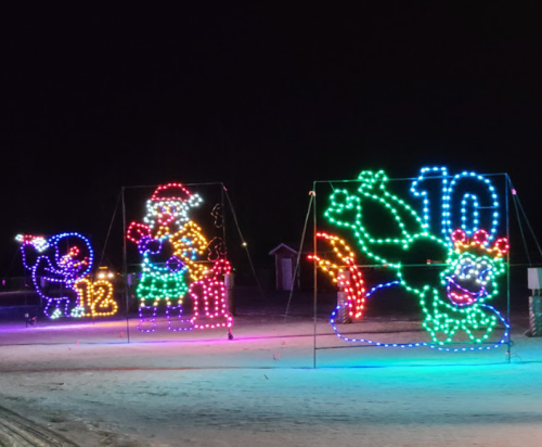Colorful holiday light displays featuring a snowman, Santa, and a dragon, set against a dark night sky.