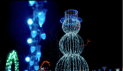 A large illuminated snowman made of lights stands against a dark background, surrounded by colorful holiday decorations.