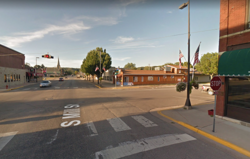 A street view of a small town intersection with flags, a stop sign, and a church steeple in the background.