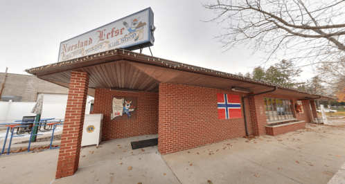 A brick building with a sign for a bakery and gift shop, featuring a Norwegian flag and autumn decorations.