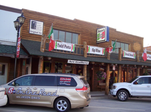 A wooden building with an art gallery sign, featuring colorful banners and a parked van in front.
