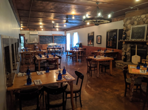 Cozy restaurant interior with wooden tables, blue glassware, and a stone fireplace, featuring a welcoming atmosphere.
