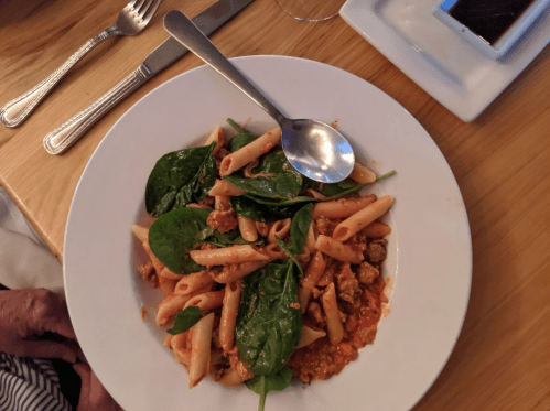 A plate of pasta with spinach and meat sauce, served with a spoon, on a wooden table.