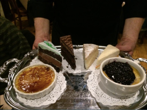 A silver tray holds various desserts: chocolate cake, cheesecake, and crème brûlée with berry compote.
