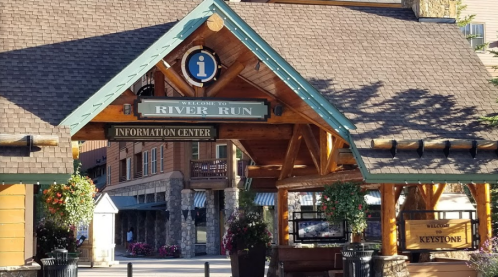 Welcome sign for River Run Information Center, featuring wooden architecture and hanging flower baskets.