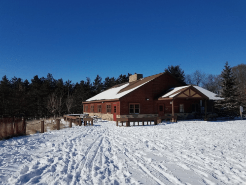 A red wooden building surrounded by snow, with a clear blue sky and trees in the background.