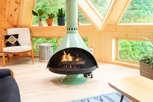 A modern green fireplace in a cozy room with large windows, plants, and stylish furniture.