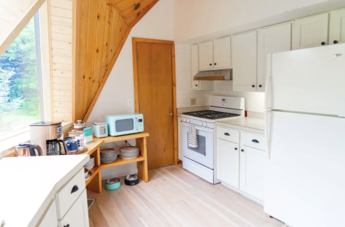 Bright kitchen with wooden accents, featuring a stove, refrigerator, microwave, and a window with a view.