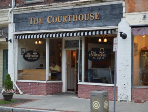 Exterior of "The Courthouse" bar and grill, featuring a striped awning and a cozy interior visible through the windows.