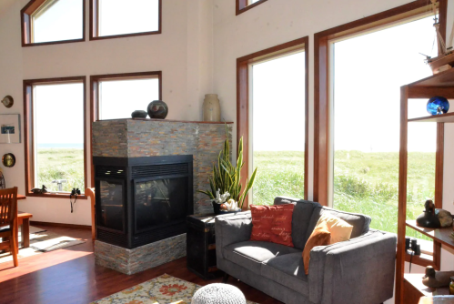 Cozy living room with a stone fireplace, large windows, and a view of greenery outside.