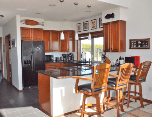 Modern kitchen with wooden cabinets, black appliances, and a breakfast bar with four high stools. Bright and spacious design.
