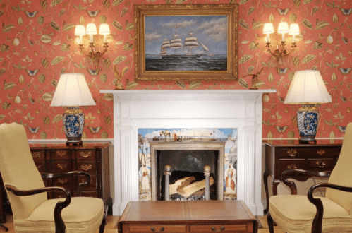 Cozy room with floral wallpaper, a fireplace, two armchairs, and a ship painting above the mantel.