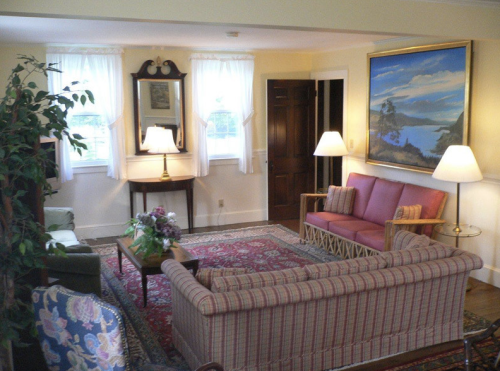Cozy living room with a pink sofa, green chair, floral decor, and a large painting, illuminated by soft lamps.