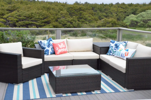 A cozy outdoor seating area with a sectional sofa, colorful pillows, and a glass coffee table on a striped rug.