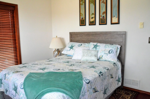 A cozy bedroom featuring a bed with a starfish-patterned quilt, a lamp, and framed artwork on the wall.