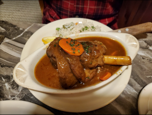 A plate featuring a braised lamb shank with carrots in a rich sauce, served with a side of rice.