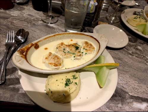 A creamy seafood dish with biscuits, served alongside a biscuit and a slice of melon on a white plate.