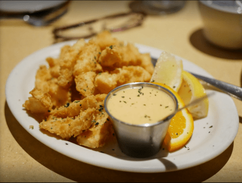 A plate of crispy fried calamari served with a creamy dipping sauce and lemon wedges.