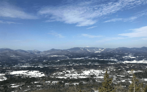A panoramic view of snow-covered mountains and valleys under a clear blue sky.