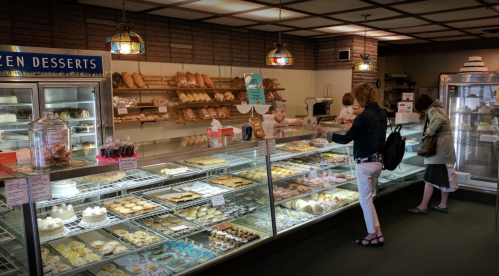 A bakery display filled with various pastries and desserts, with customers browsing and staff serving behind the counter.