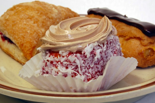 A plate with three pastries: a jelly-filled croissant, a coconut-covered cake with frosting, and a chocolate eclair.