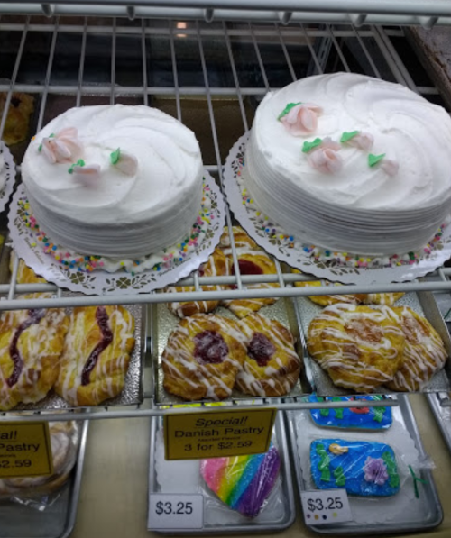 Two decorated cakes with white frosting and flowers, alongside assorted pastries in a display case.