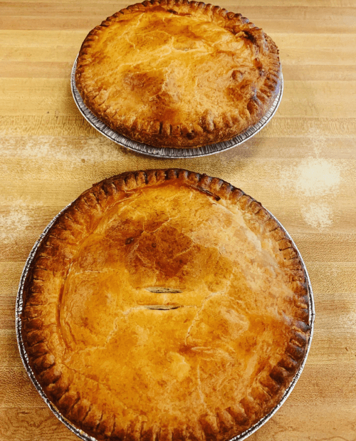 Two golden-brown pies with flaky crusts, resting on a wooden surface.
